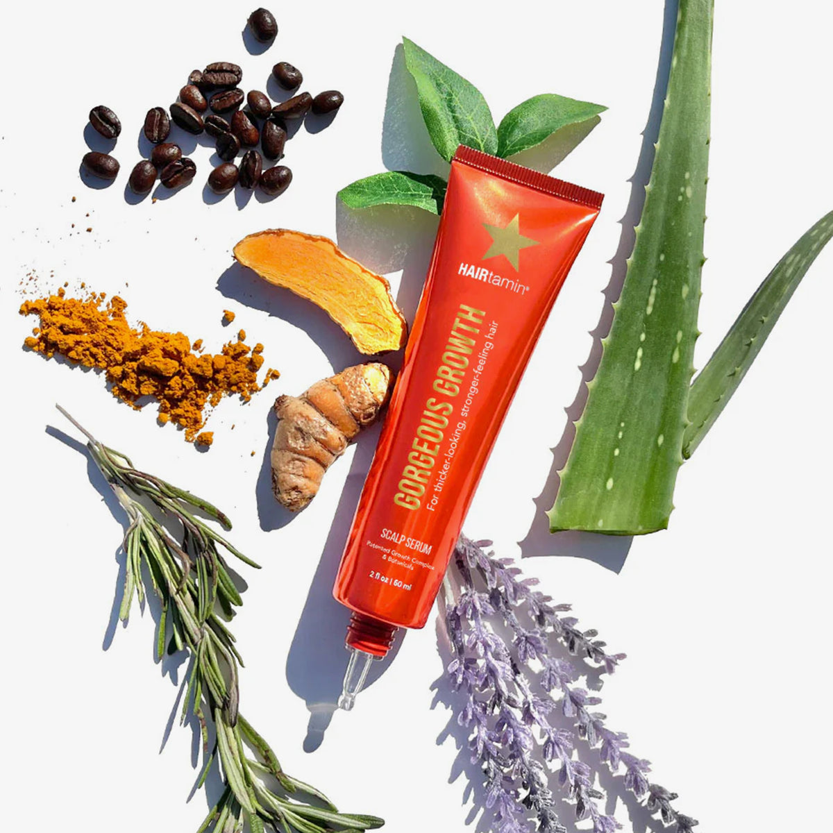 Eine rote Tube Scalp Serum von HAIRtamin ist von Kurkuma, Kaffeebohnen, Aloe, Lavendel und grünen Blättern umgeben.