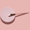 Der K1: Eye & Lip Glitter Pigment Brush in Pink liegt auf einem runden pinkfarbenen Zylinder, auf einem rosafarbenen Hintergrund.
