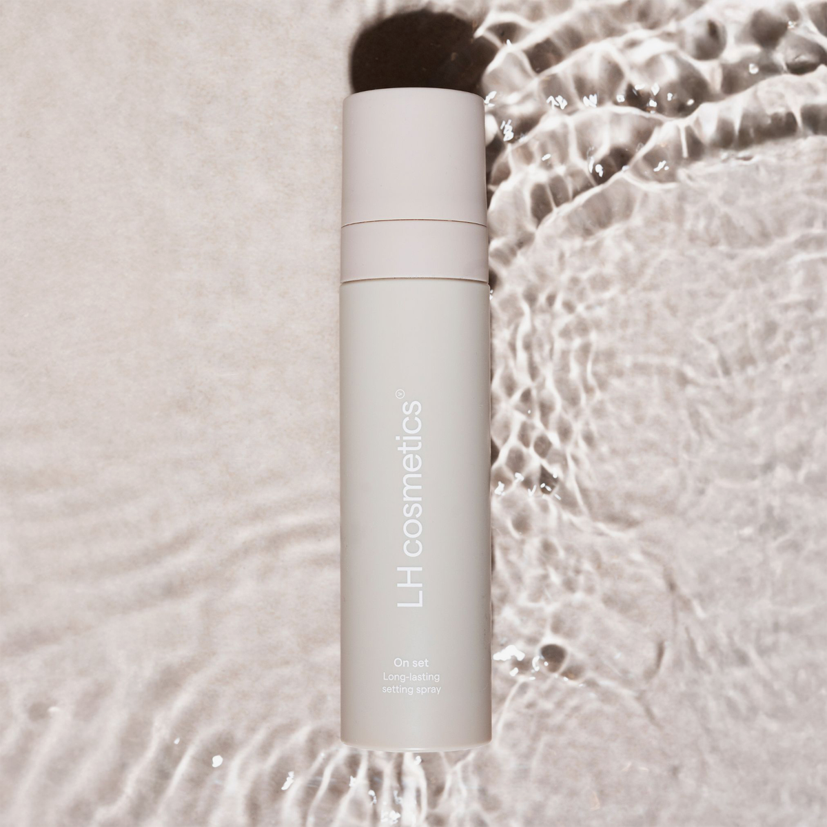 Beige Flasche LH Cosmetics On Set – Long Lasting Setting Spray auf einer Wasserfläche.
