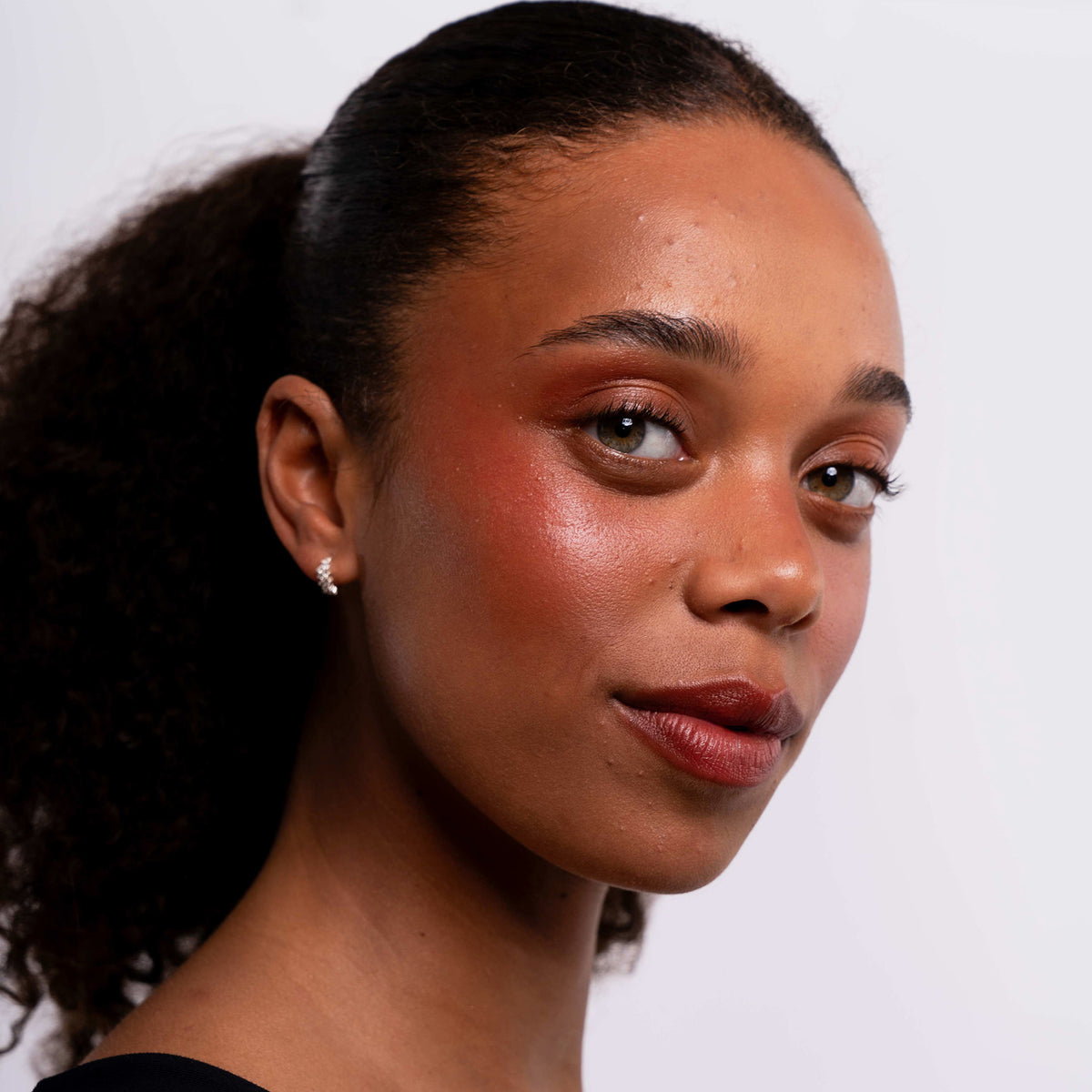 Eine Frau mit lockigem Haar trägt LH Cosmetics Artistick Blush Canvas und natürliches Make-up.