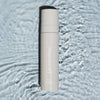 Eine Flasche LH Cosmetics On Set – Subtle Glow Setting Spray steht auf plätscherndem, reflektierendem Wasser.