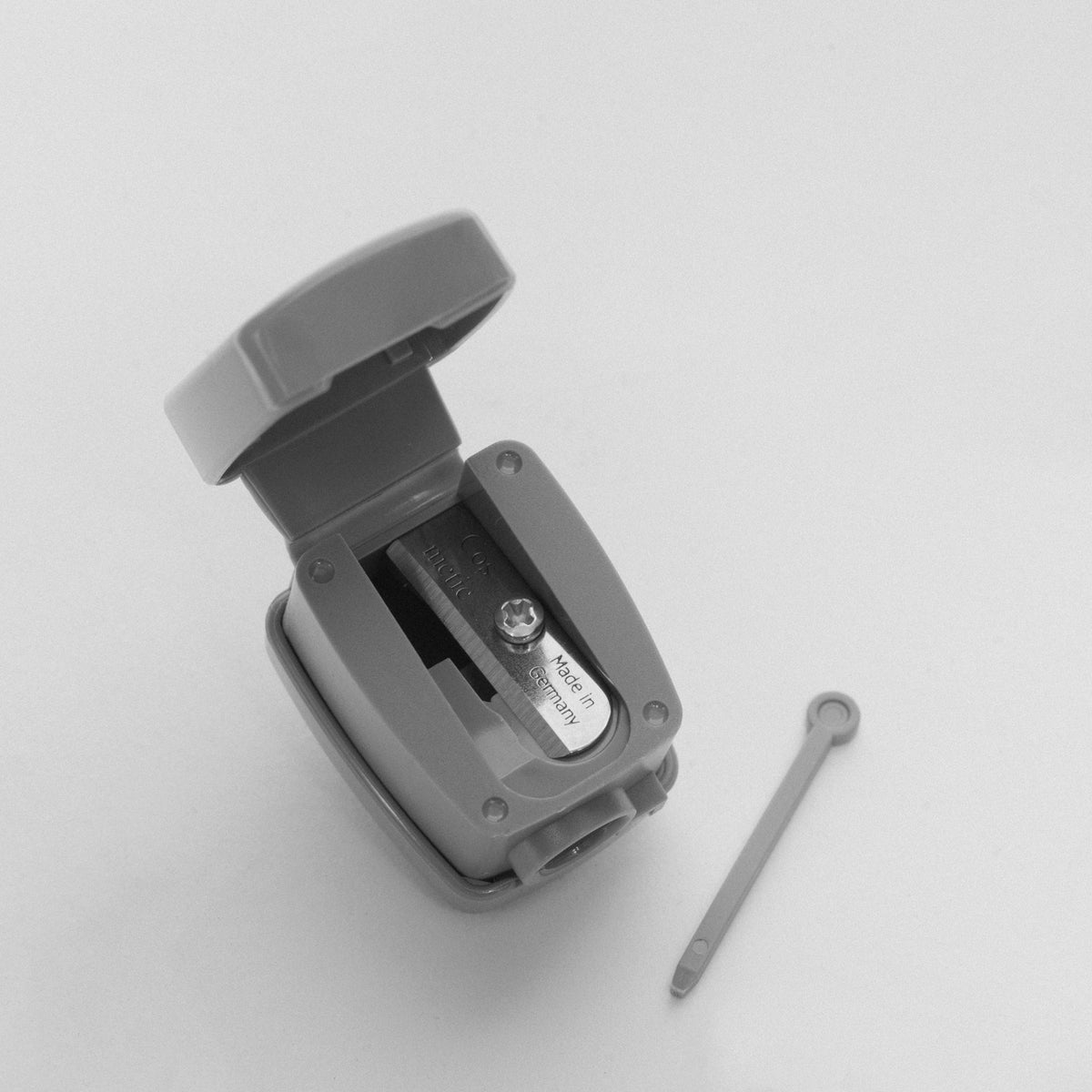 Auf weißem Hintergrund ist der LH Cosmetics Sharpe diem Sharpener abgebildet, ein Spitzer aus Kunststoff mit offenem Deckel und einem kleinen Reinigungsstab daneben.