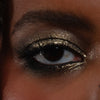 Nahaufnahme eines Auges mit intensivem Make-up in schimmerndem Olivgold und Schwarz, das auf dem Lid und entlang des unteren Wimpernkranzes aufgetragen ist.
