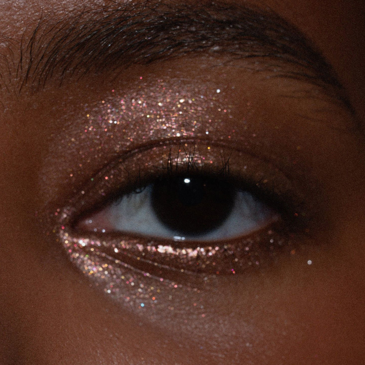 Nahaufnahme eines Auges mit glitzerndem Lidschatten in Rosé- und Goldtönen auf dem Lid und unteren Wimpernkranz.