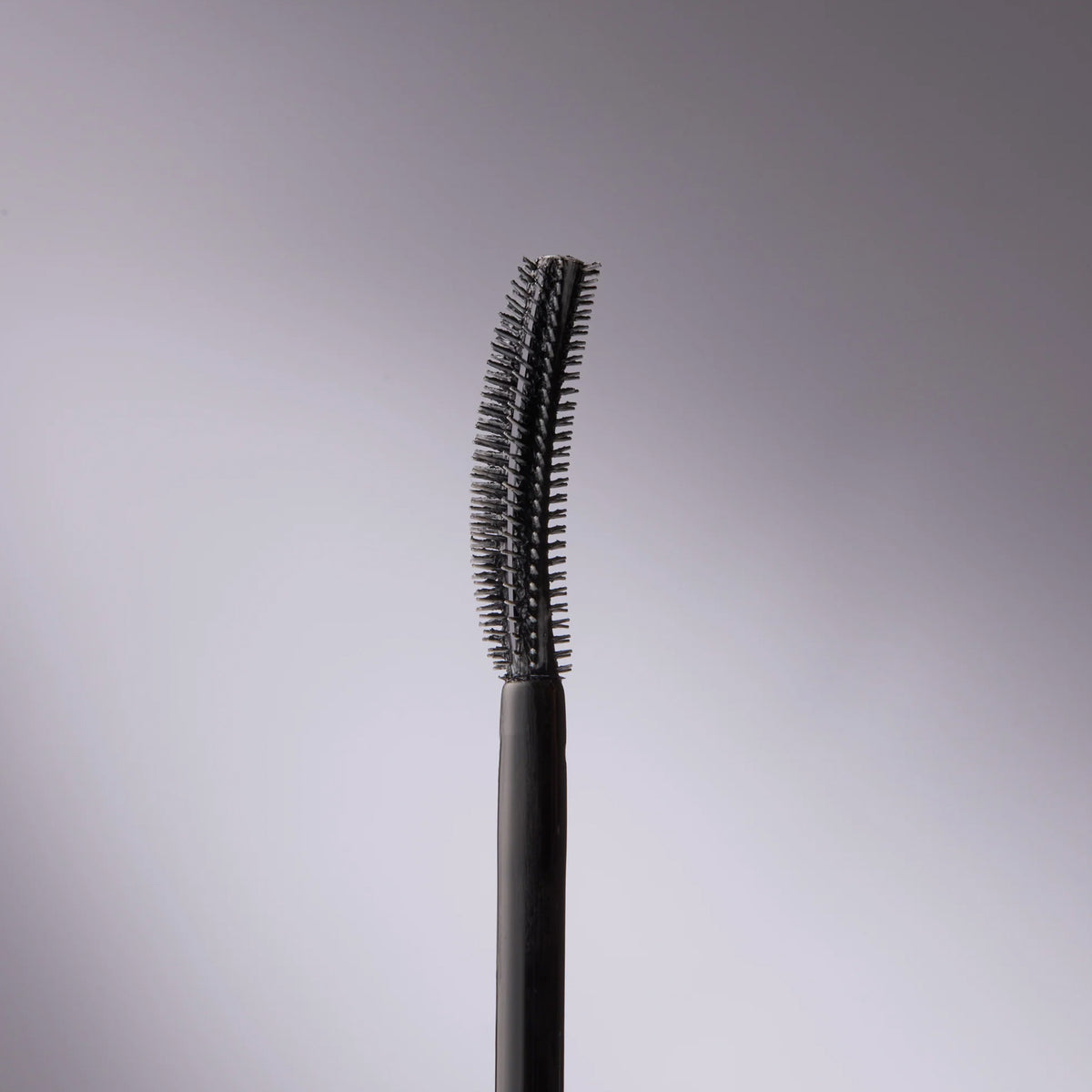 Der Applikator der Femuline™ Mascara von Mesauda Beauty zeichnet sich durch einen schwarzen, geschwungenen Kopf aus, vor grauen Hintergrund mit Verlauf.