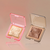Das NABLA Cosmetics Illuminating Bundle enthält zwei quadratische Kompaktdosen mit strukturierten Pudern - eine hellgoldene und eine bronzefarbene - in klaren Kunststoffhüllen.