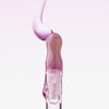 Ein Tropfen Lip Candy Oil in Lila gleitet vor einem hellrosa Hintergrund über den Applikator.