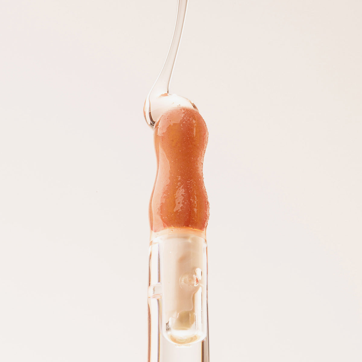 Ein Tropfen Lip Candy Oil in der Farbe Honey gleitet vor einem pfirsichfarbenem Hintergrund über den Applikator.