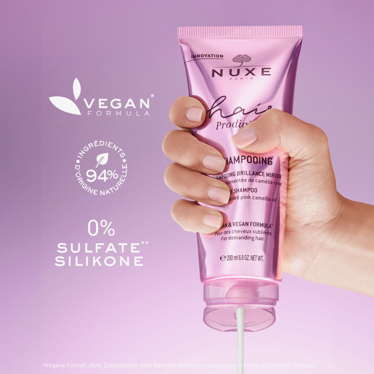 Eine Hand hält eine rosa Tube NUXE Hair Prodigieux Glanz-Shampoo mit der Aufschrift „vegan“, „94 % natürlichen Ursprungs, 0 % Sulfat und Silikon“.