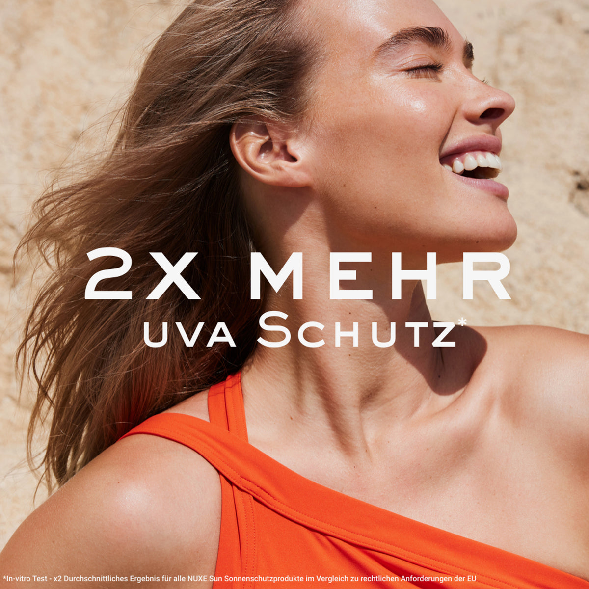 Frau mit geschlossenen Augen und orangefarbenem Top in der Sonne, Text „2x mehr UVA-Schutz*“ im Vordergrund, vor sandigem Hintergrund.
