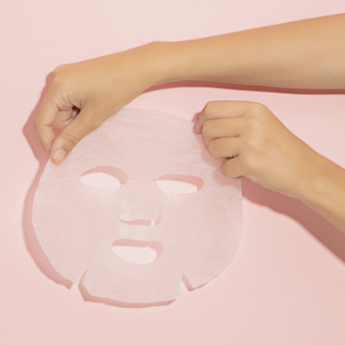 Hände halten die Adenosine & Zhi Mu Lifting Mask Tang-Tang-Tuchmaske vor einem rosa Hintergrund.