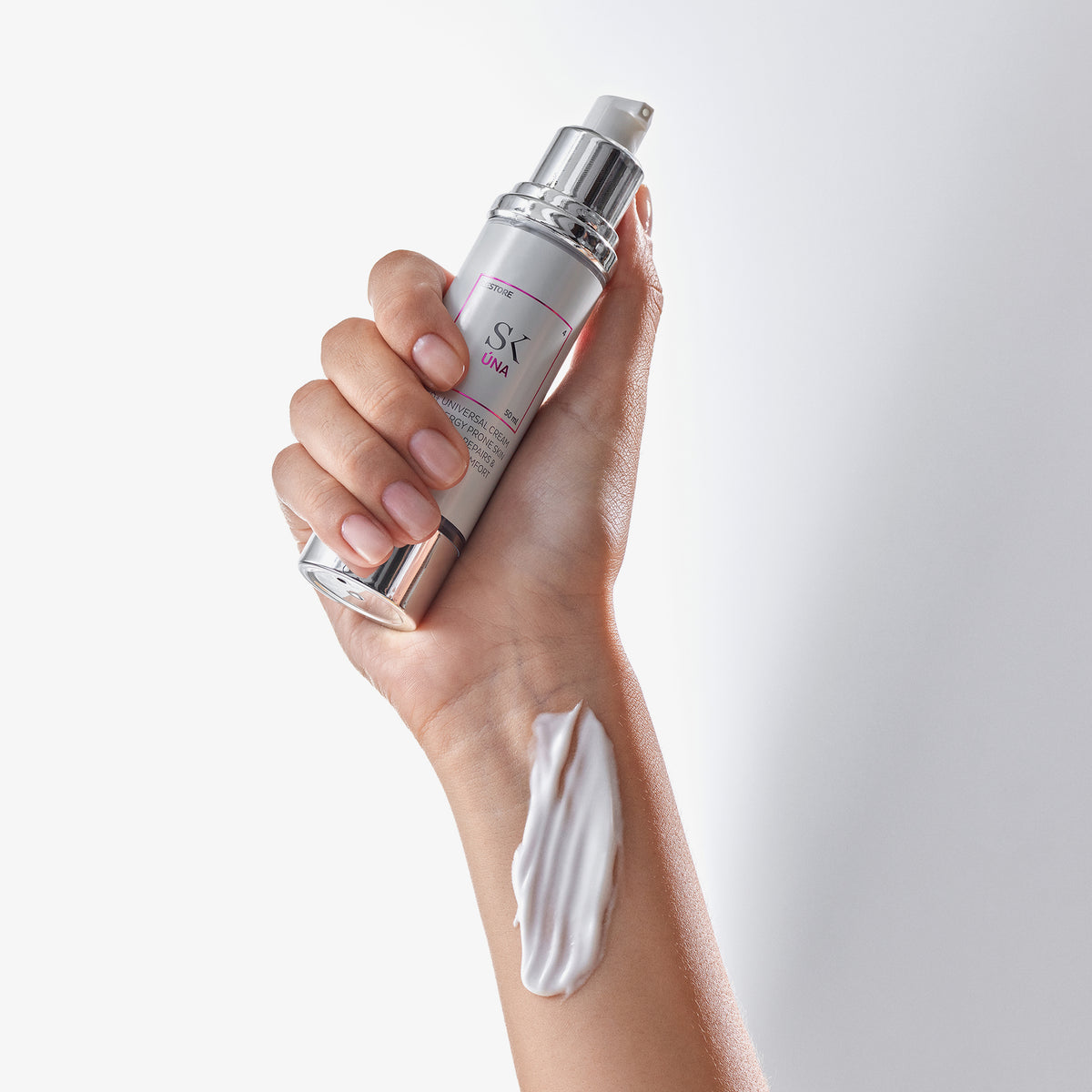 Eine Hand hält vor einem weißen Hintergrund eine Úna-Hautpflegeflasche mit Creme auf dem Unterarm.