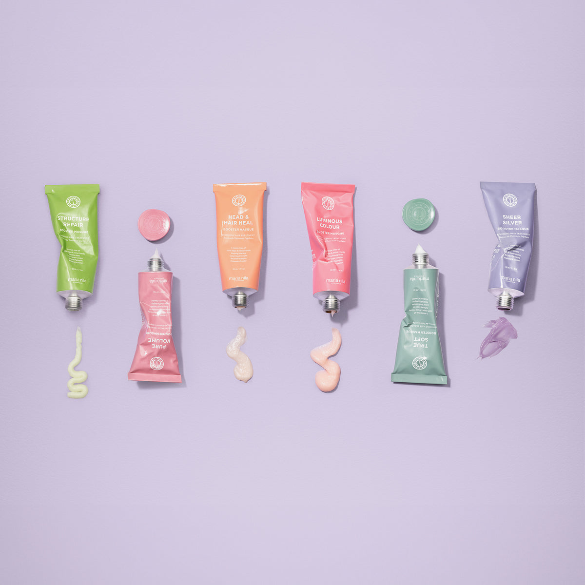 Sechs bunte Tuben maria nila Booster Masque True Sof  mit passenden Deckeln und Cremeswatches auf einem lavendelfarbenen Hintergrund.
