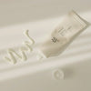 Offene Tube Relief Sun: Rice + Probiotics liegt auf einer hellen Oberfläche, daneben wirft ein cremefarbener Swatch der Lotion
