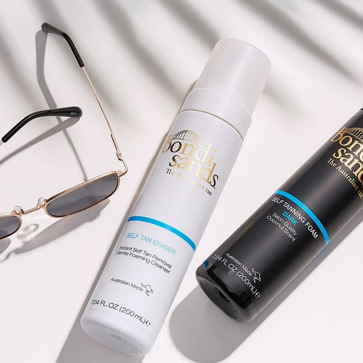 Der Bondi Sands Self Tan Eraser und der Self Tanning Foam Dark neben einer Sonnenbrille auf weißem Hintergrund.