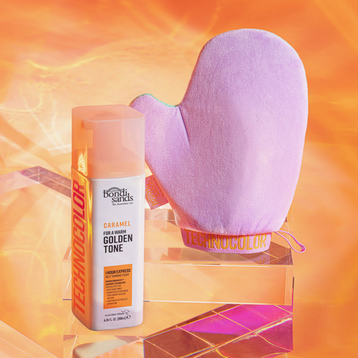 Technocolor 1 Hour Express Self Tanning Foam Caramel neben violettem Handschuh auf durchsichtigen Blöcken vor einem orangefarbenen Hintergrund.