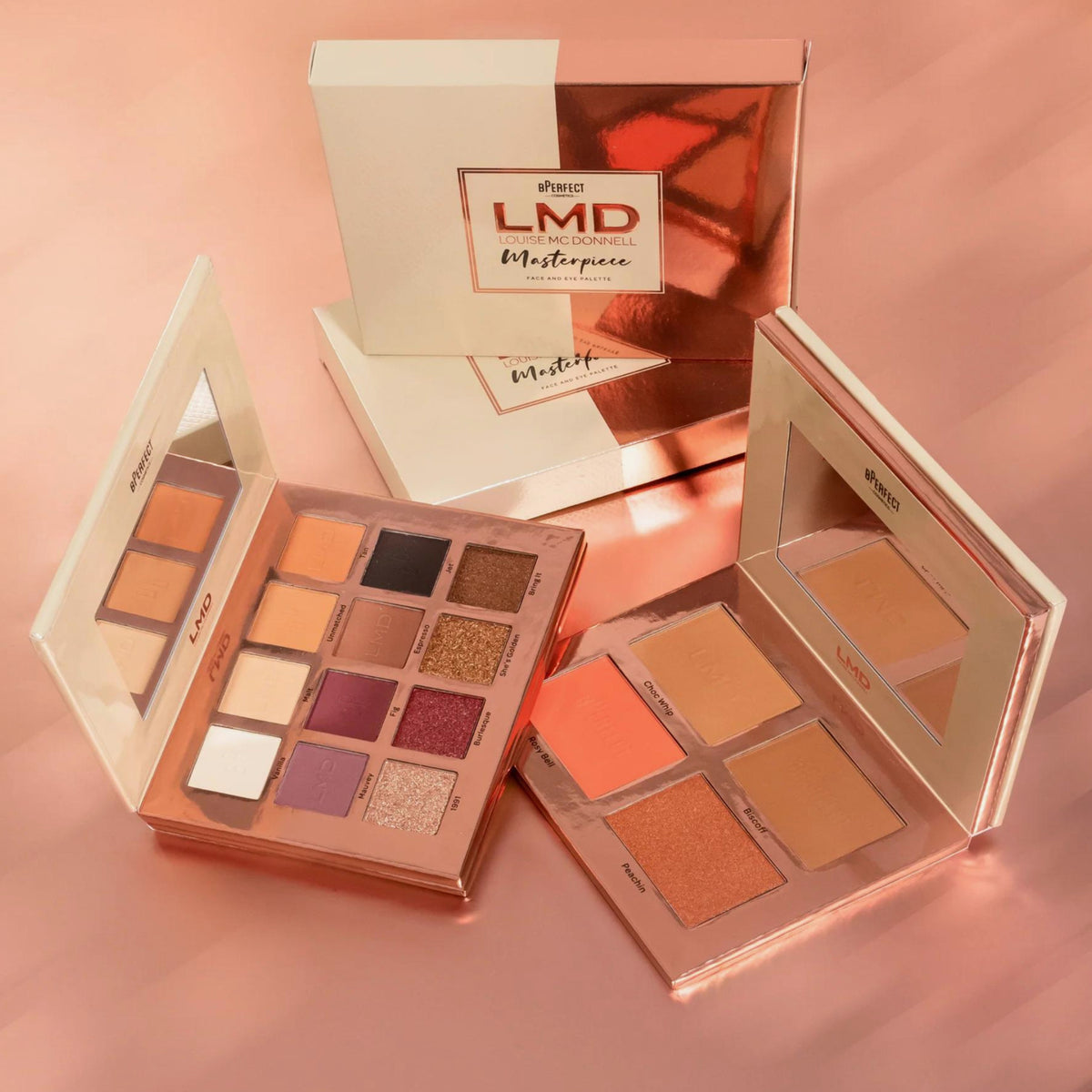 BPerfect Cosmetics x LMD Masterpiece Face & Eye Palette offen auf einer rosa Oberfläche; Verpackung im Hintergrund sichtbar