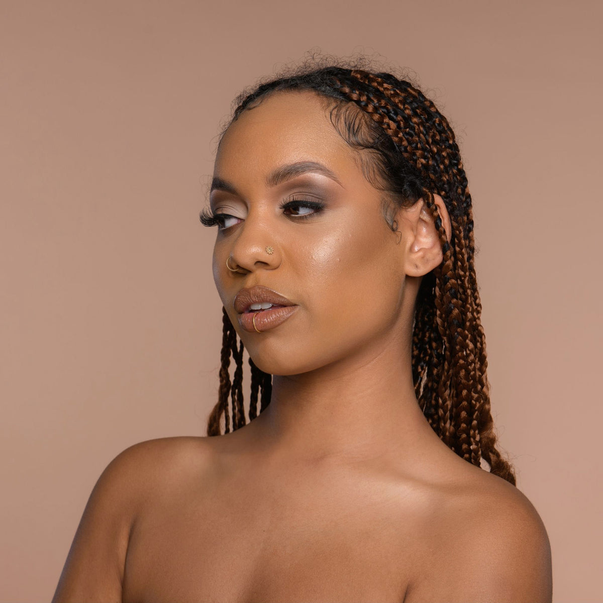 Person mit geflochtenem Haar und neutralem Make-up zeigt den Cronzer Cream Bronzer Acron vor beigem Hintergrund.