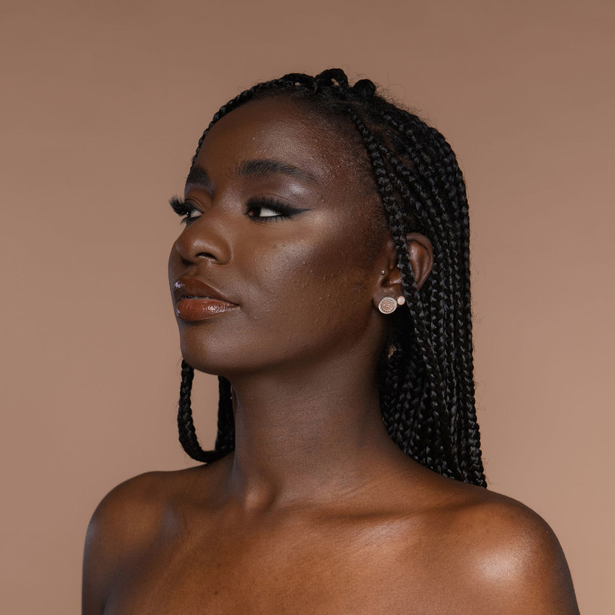 Person mit geflochtenem Haar und neutralem Make-up zeigt den Cronzer Cream Bronzer Fig vor beigem Hintergrund.