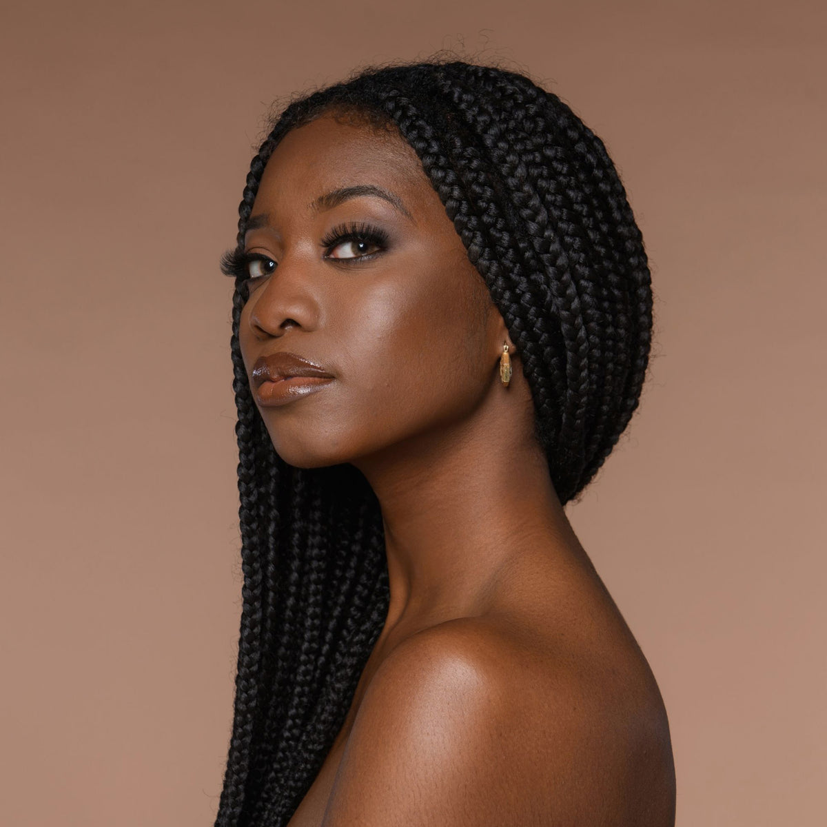 Person mit geflochtenem Haar und neutralem Make-up zeigt den Cronzer Cream Bronzer Nutty vor beigem Hintergrund.