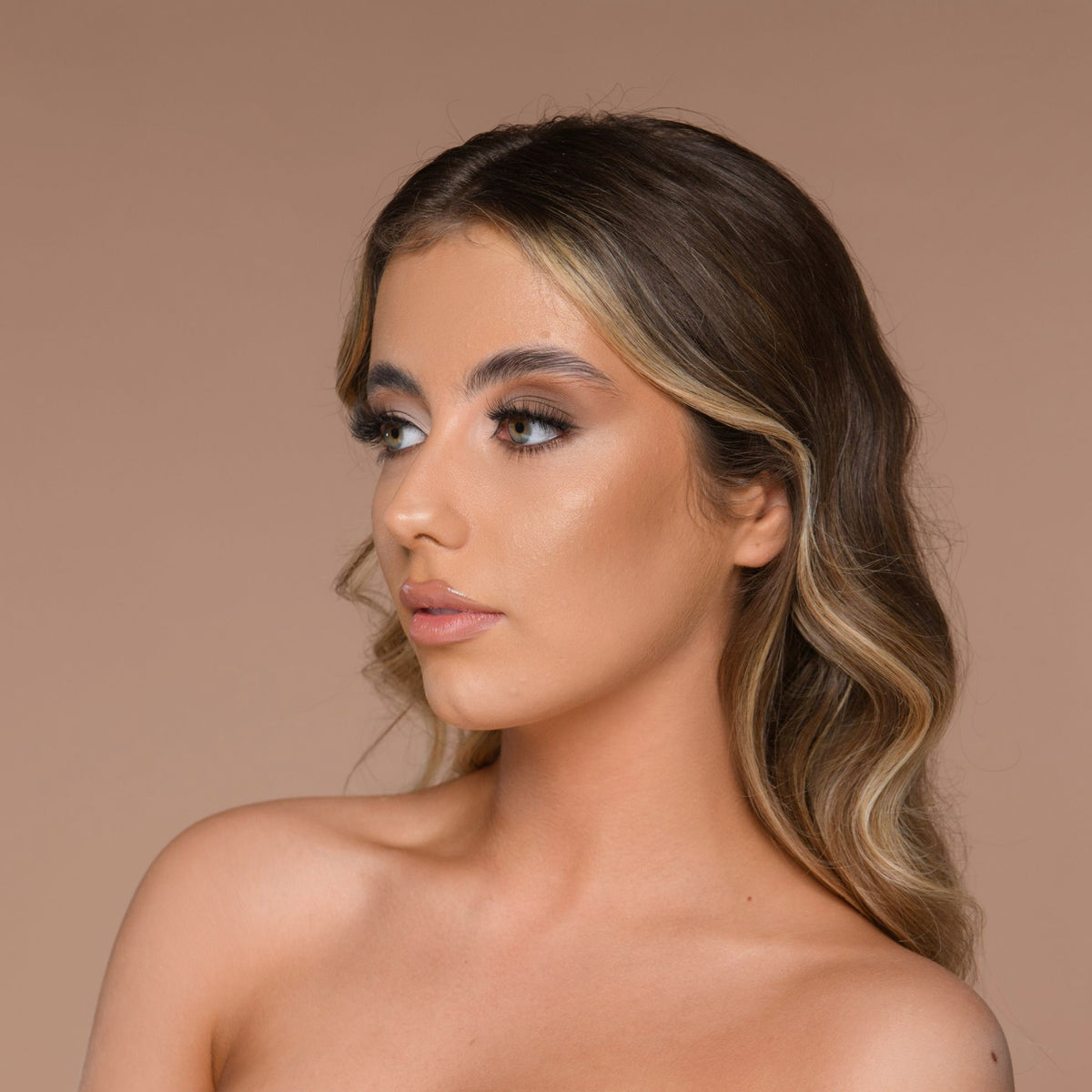 Eine Frau mit welligem Haar blickt vor einem neutralen Hintergrund nach rechts und präsentiert Cronzer – Cream Bronzer.