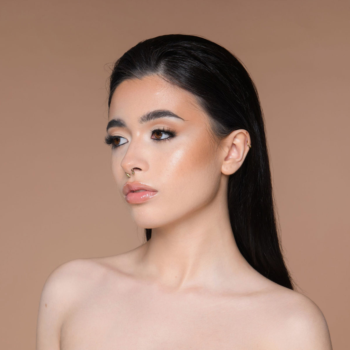 Eine Frau mit langem dunklem Haar, neutralem Make-up und nackten Schultern posiert vor einem beigen Hintergrund, hervorgehoben durch Cronzer – Cream Bronzer.