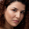 Eine Frau mit lockigem Haar und Creolen blickt in die Kamera und präsentiert den Melted Sun Liquid Bronzer 015.