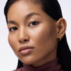 Eine Frau mit glattem Haar und goldenen Ohrringen blickt in die Kamera und präsentiert den Melted Sun Liquid Bronzer 025.