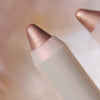 Nahaufnahme eines PEARLFECTION Eyeshadow Sticks in metallischem Roségold vor einem weichgezeichneten Hintergrund.