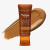 Eine Tube Yummy Skin Serum Tint 1 vor einem warmem braunem Farbmuster.