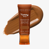 Eine Tube Yummy Skin Serum Tint 13 vor einem warmem dunkelbraunem Farbmuster.