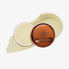 Runde geöffnete bronzefarbene Dose des Yummy Skin Blurring Balm Powder vor einem Farbstreifen der Shade Universal.