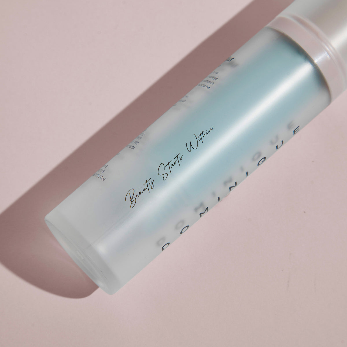 Mattierte Flasche „Cooling Blur Mattifying Primer“ mit dem Text „Beauty Starts Within …“, auf einer blassrosa Oberfläche liegend.