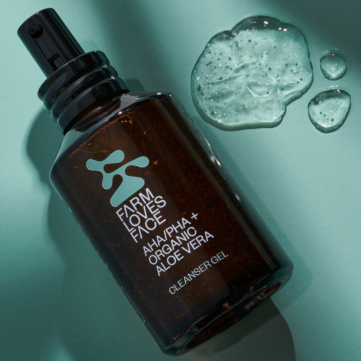 Eine Flasche AHA/PHA + Organic Aloe Vera Cleanser Gel mit Gelklecksen liegt auf einer türkisen Oberfläche.