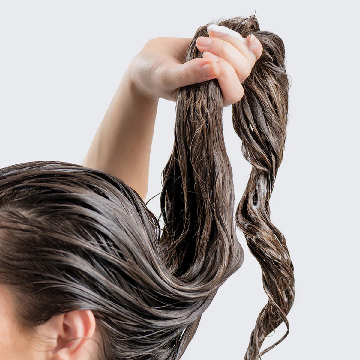 Eine Person hält ihr langes, nasses, mit dem Shampoo & Conditioner Duo Pack behandeltes Haar hoch.