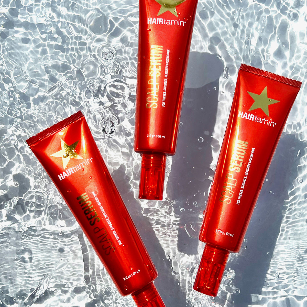Drei Flaschen HAIRtamin Scalp Serum schwimmen in klarem, plätscherndem Wasser.