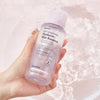 Eine Hand hält eine Flasche Real Complexion Hyaluron Skin Essence über spritzendes Wasser.