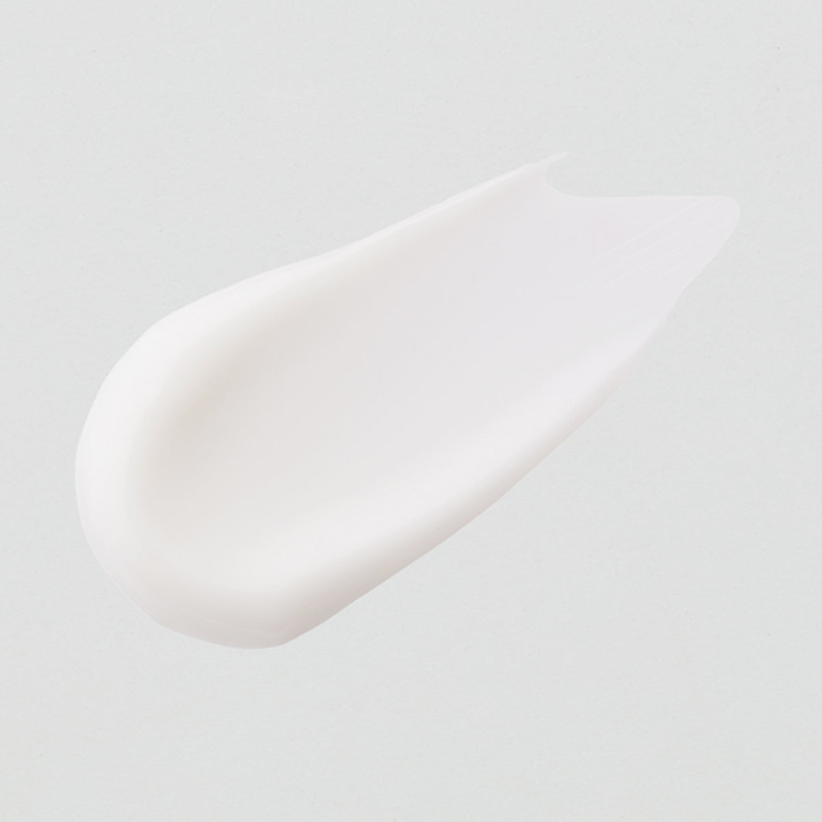 Ein glatter Fleck der weißen Textur der Vitamin A Glow Retinol Cream auf hellgrauem Hintergrund.