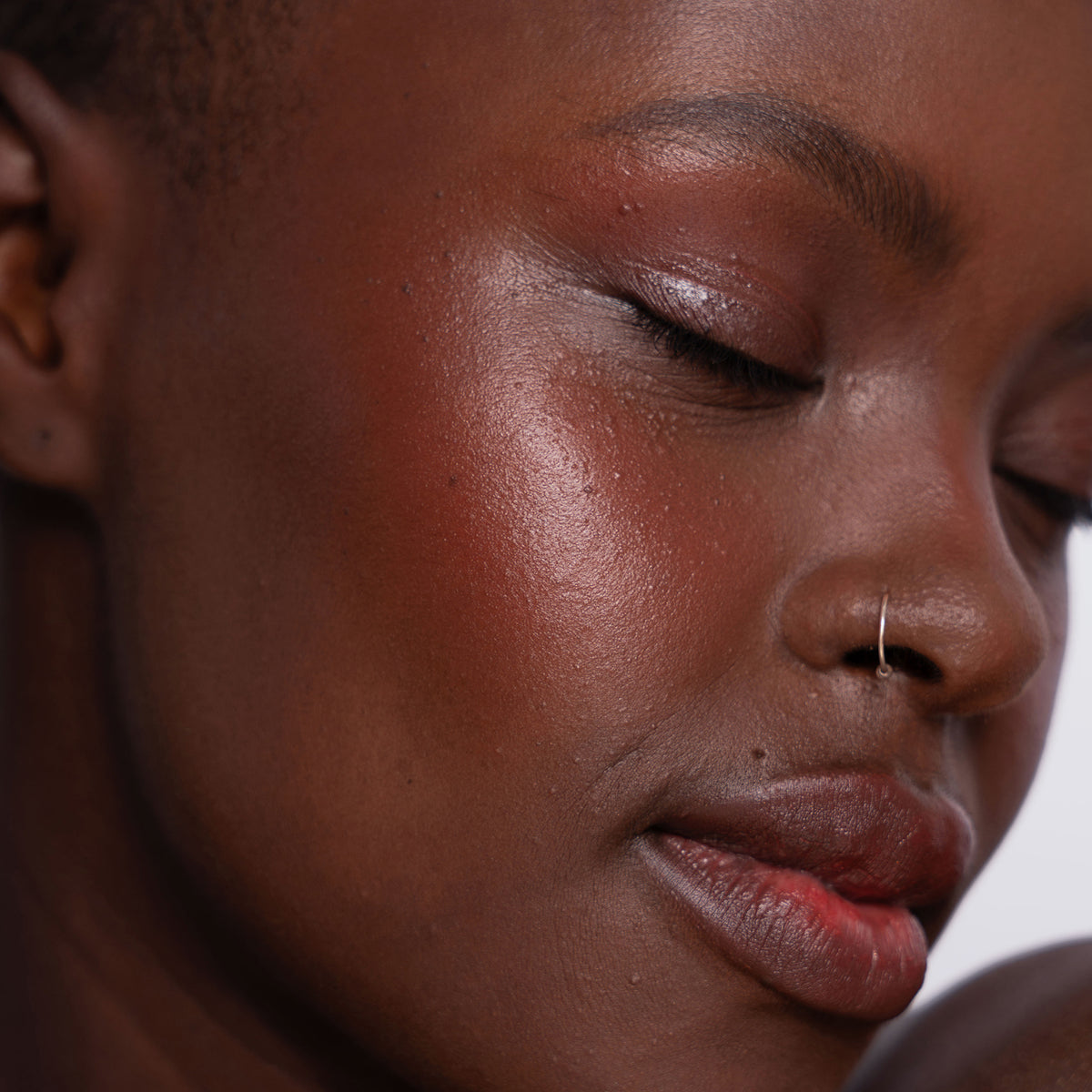 Nahaufnahme einer Frau mit strahlender dunkler Haut, dezentem Make-up und einem Nasenring, die Artistick Blush Canvas von LH Cosmetics trägt.