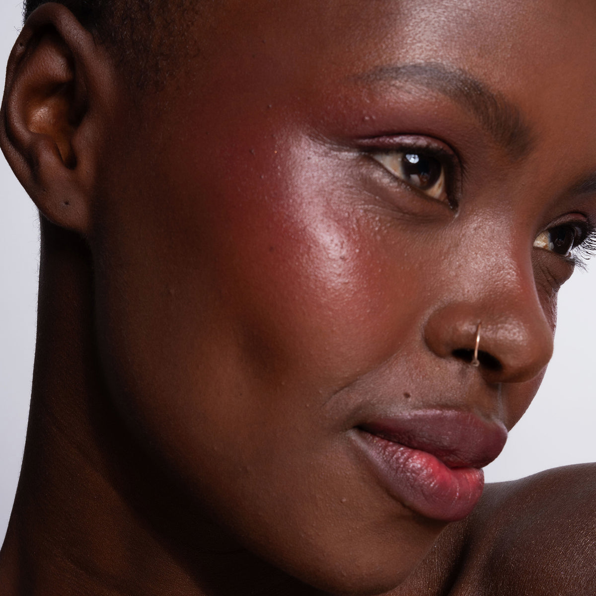 Nahaufnahme der strahlenden dunklen Haut einer Frau, betont durch LH Cosmetics Artistick Blush Stroke in Pink.