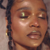 Eine Person mit geflochtenem Haar, einem Nasenring und geschlossenen Augen zeigt ein strahlendes, schimmerndes Make-up, das mit LH Cosmetics Aurora kreiert wurde.