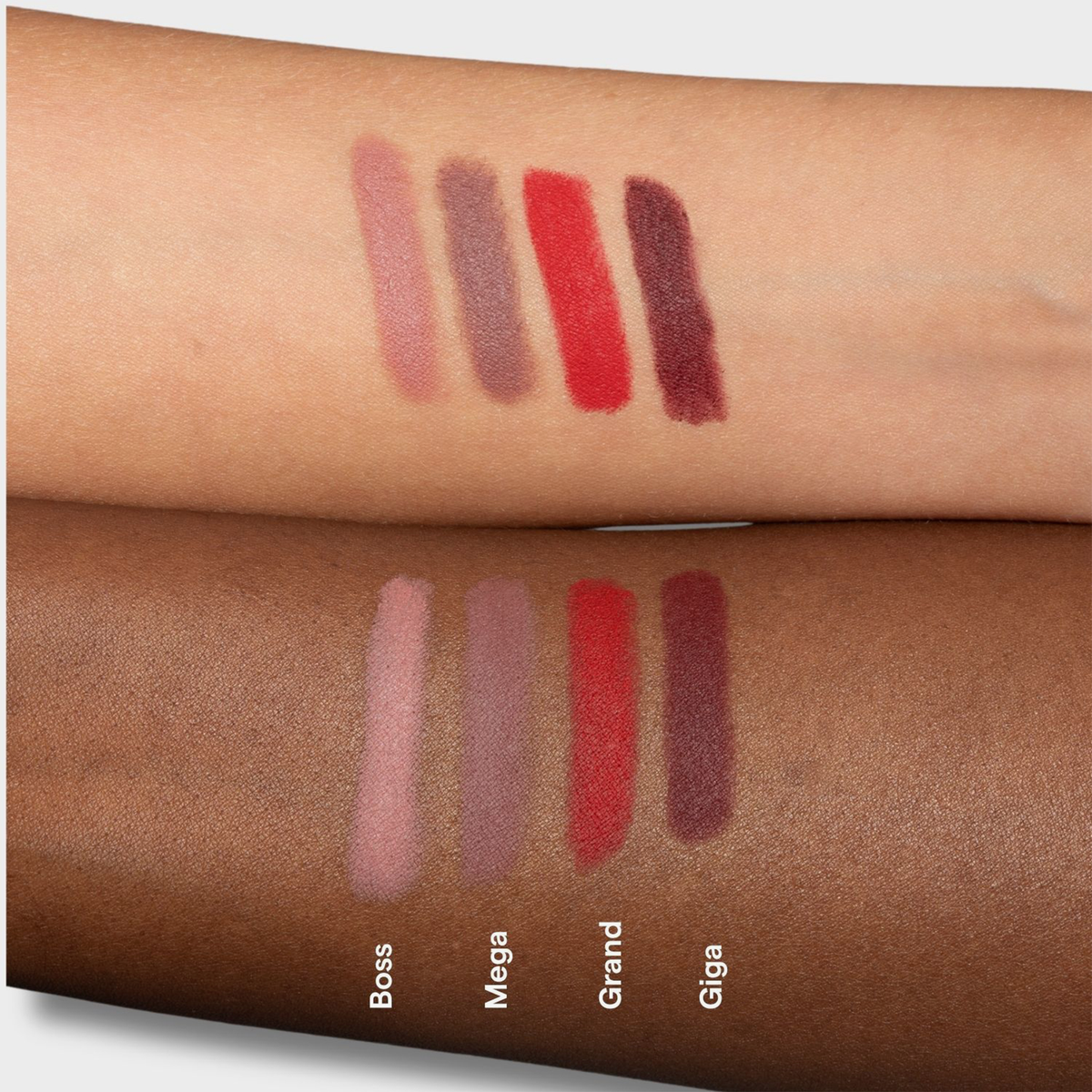 Vier LH Cosmetics Biggie-Lippenstiftproben mit den Bezeichnungen Boss, Mega, Grand und Giga auf hellen und dunklen Hautarmen.