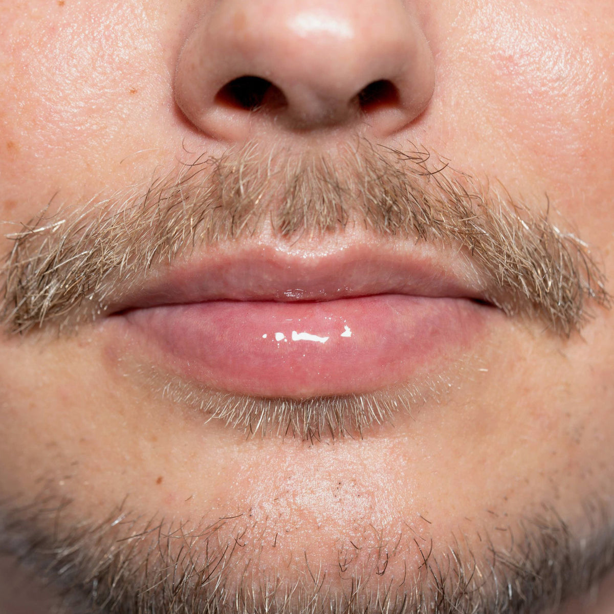 Nahaufnahme der Lippen und des Barts einer Person mit glänzendem Lippenöl "Gloil" von LH Cosmetics.