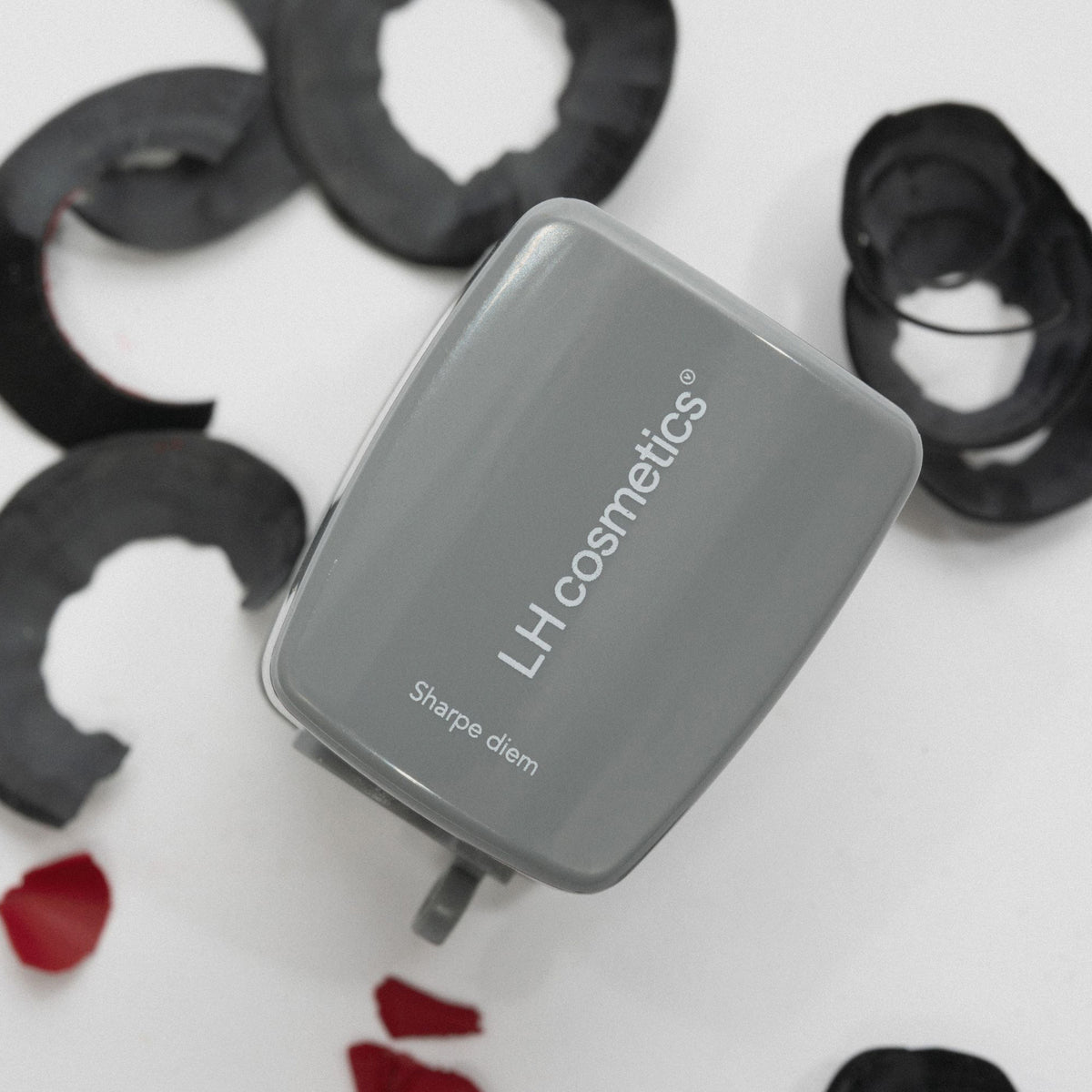 Der Sharpe Diem Sharpener von LH Cosmetics liegt auf einer weißen Oberfläche, umgeben von Kajalstiftspänen.
