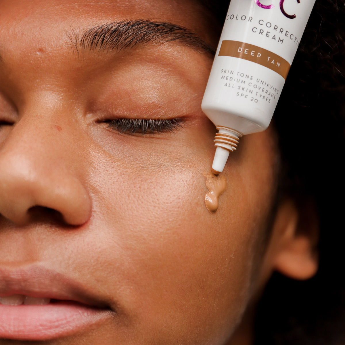 Nahaufnahme einer Person mit mittlerem Hautton, die mit geschlossenen Augen die Lumene CC Color Correcting Cream SPF20 Deep Tan auf ihre Wange aufträgt.
