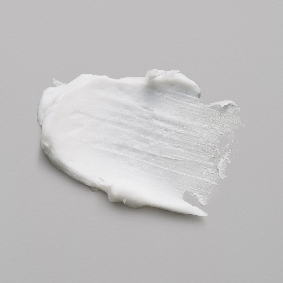 Ein weißer Abstrich der maria nila Gabbro Fixating Wax auf einer hellgrauen Oberfläche.