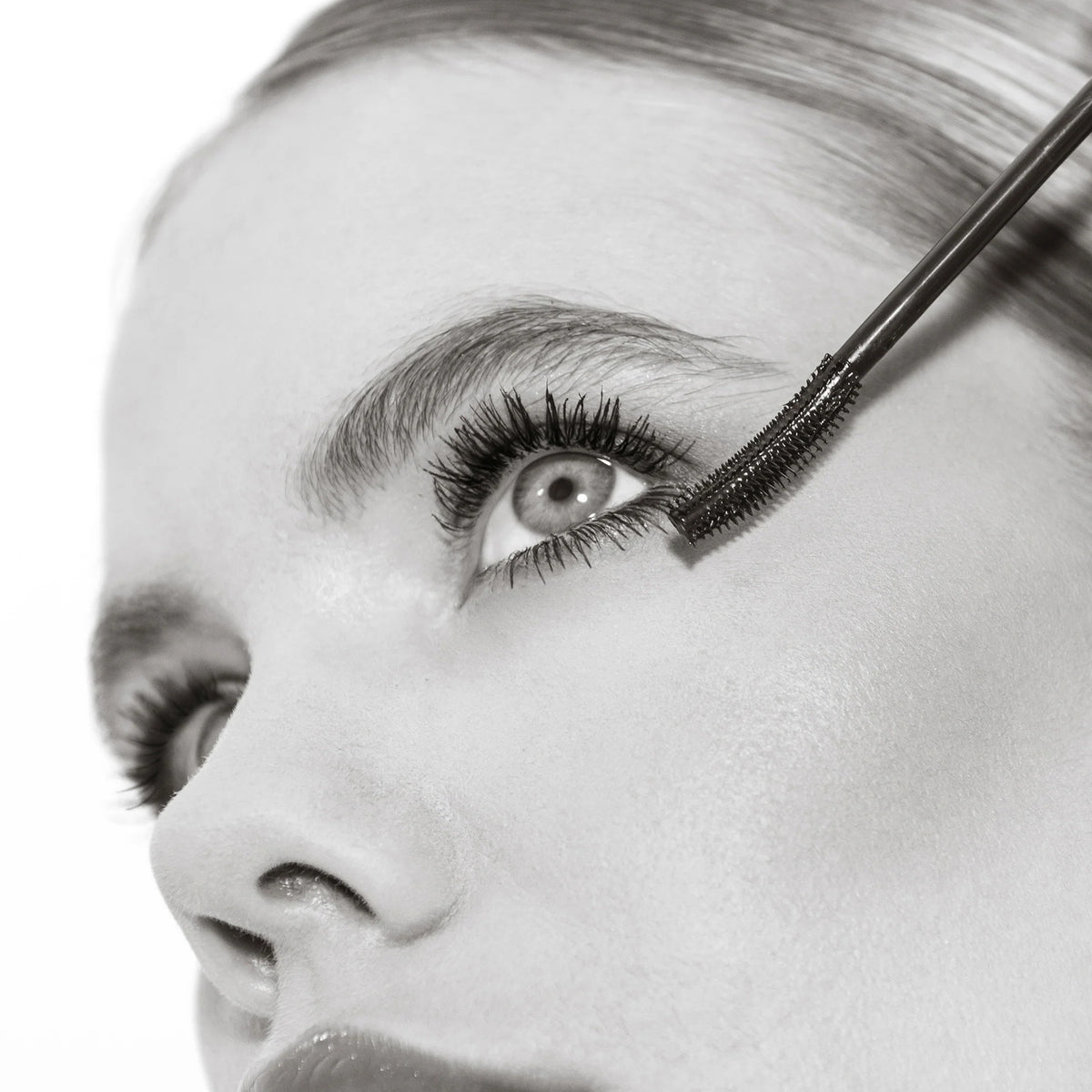 Eine Nahaufnahme zeigt, wie eine Frau die Femuline™ Mascara von Mesauda Beauty mit einer gebogenen Bürste auf ihre oberen Wimpern aufträgt.