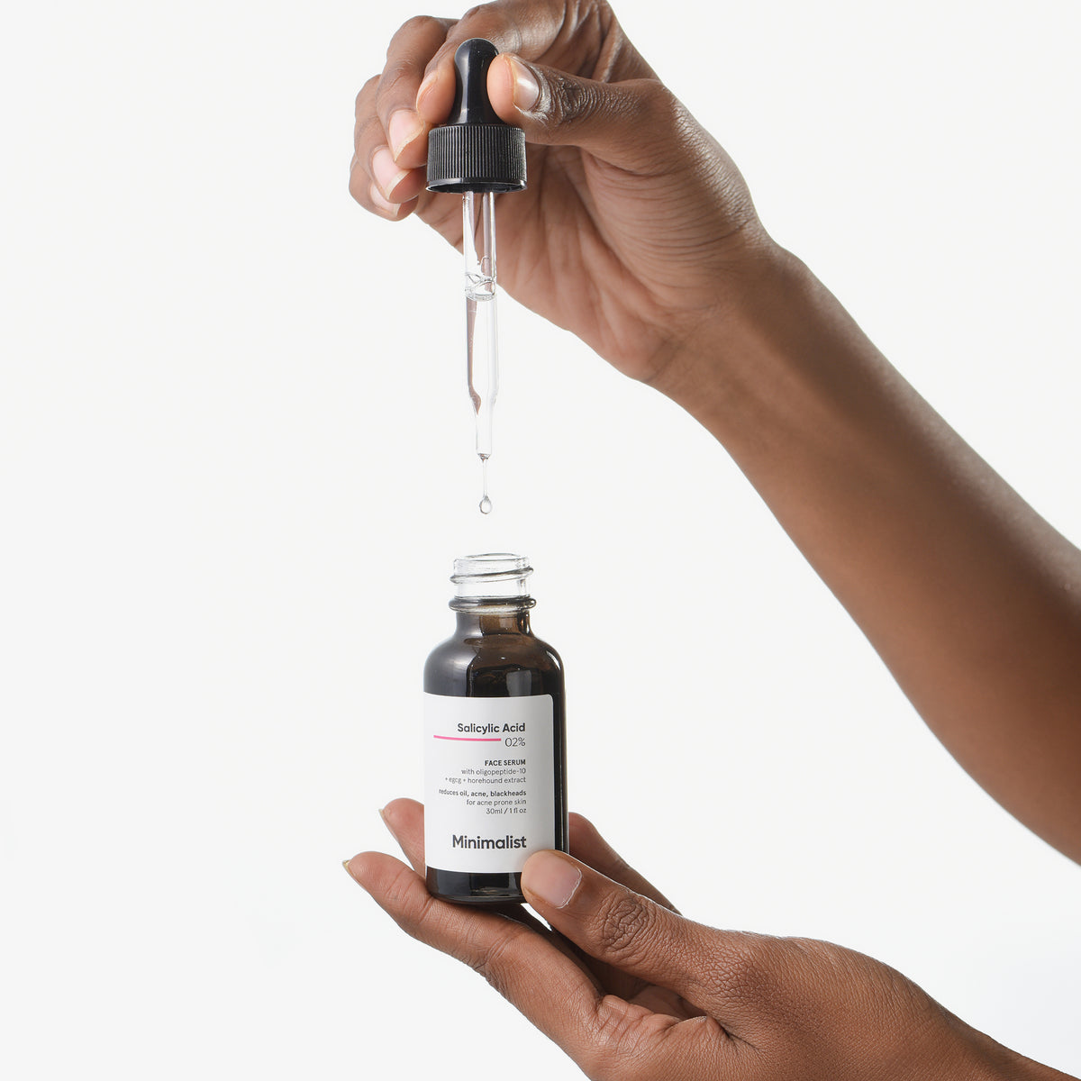 Eine Person hält eine Flasche und eine Pipette mit Salicylsäure-Gesichtsserum 0,2 % in der Hand, aus der ein Tropfen fällt.