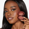 Eine Frau mit leichtem Make-up hält das Close-Up Blurring Powder Blush Compact an ihr Gesicht und präsentiert das Produkt.