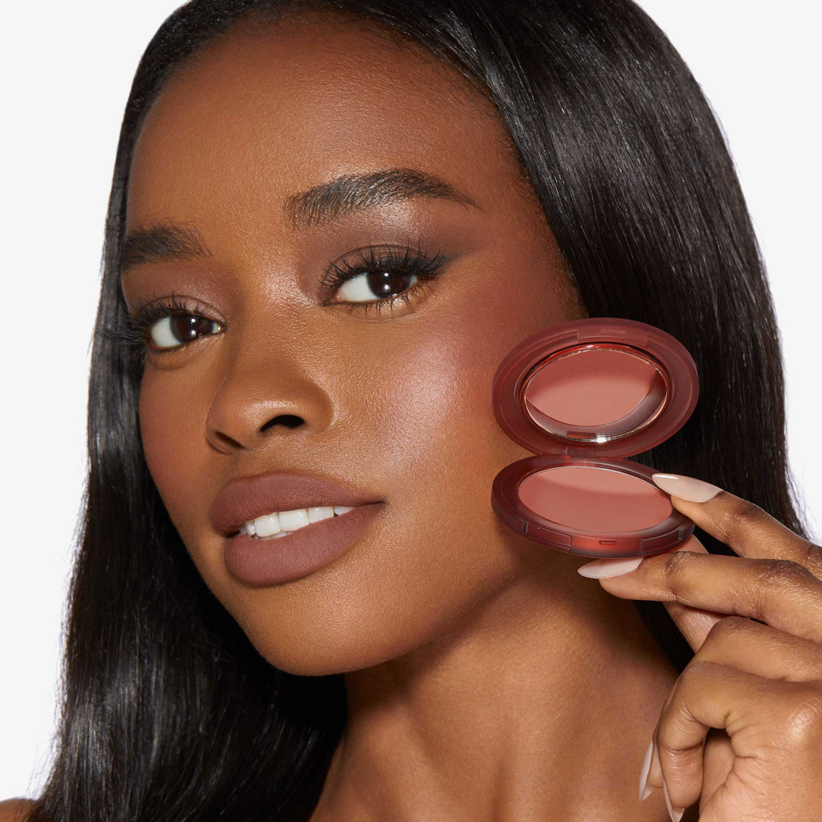 Eine Frau mit leichtem Make-up hält das Close-Up Blurring Powder Blush Compact an ihr Gesicht und präsentiert das Produkt.